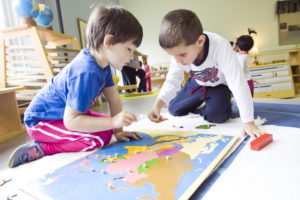 Two children are playing with a map of the world.