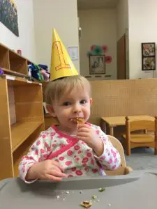 A child wearing a birthday hat eating some food.