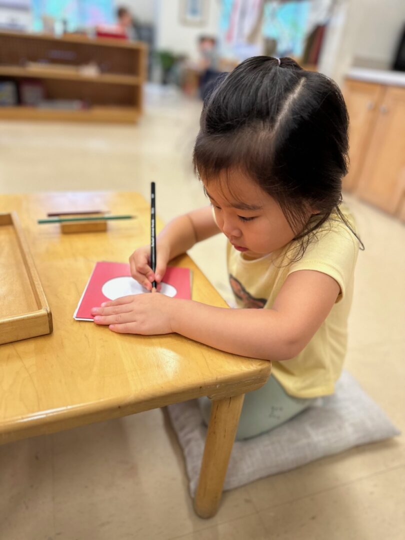 A little girl sitting at the table writing on paper.