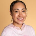 Smiling person in pink hoodie, peach background.